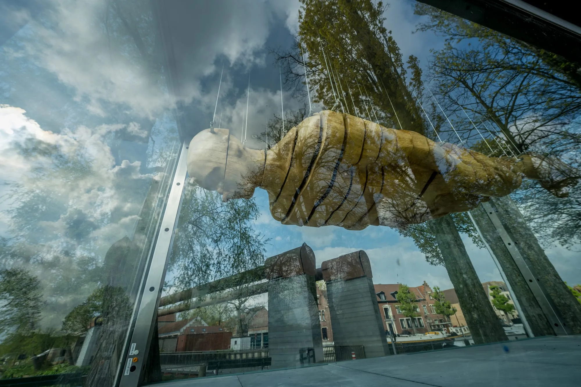 A sculptural fist suspended in a glass façade, reflecting a Bruges canal and historic gables