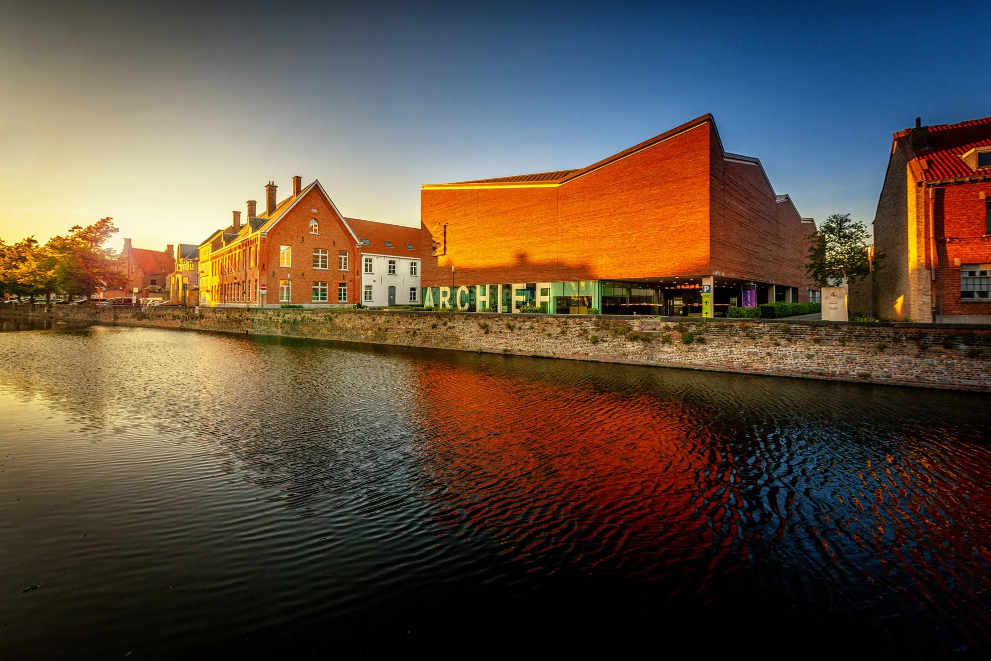 The Bruges city archive building at golden hour, mirrored in the canal