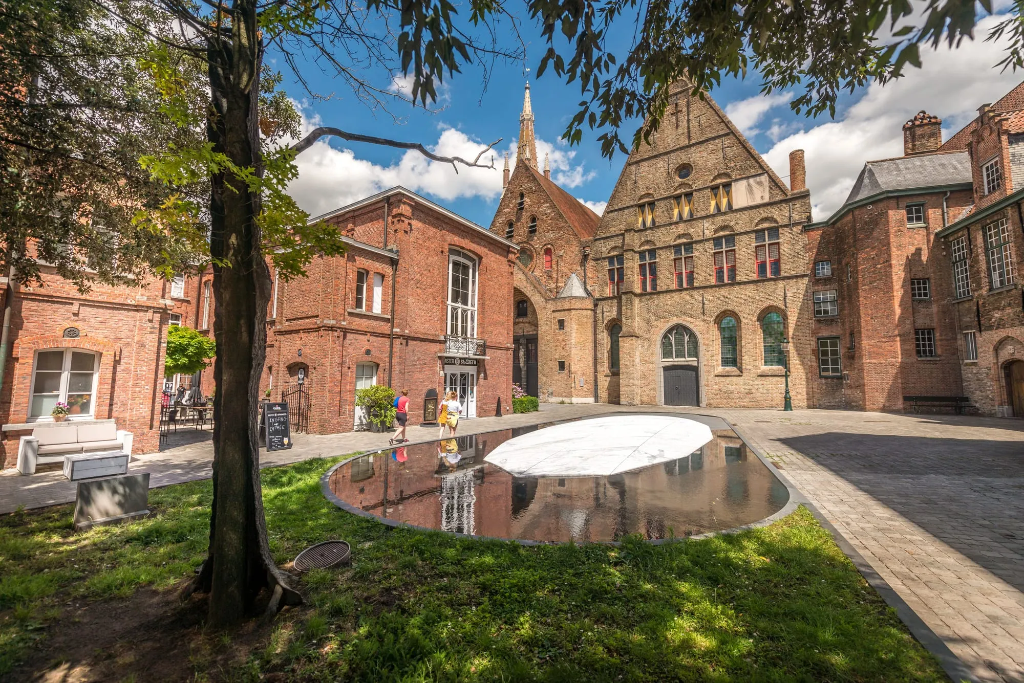 Sunny red-brick courtyard with a mirror-finish oval sculpture on the lawn