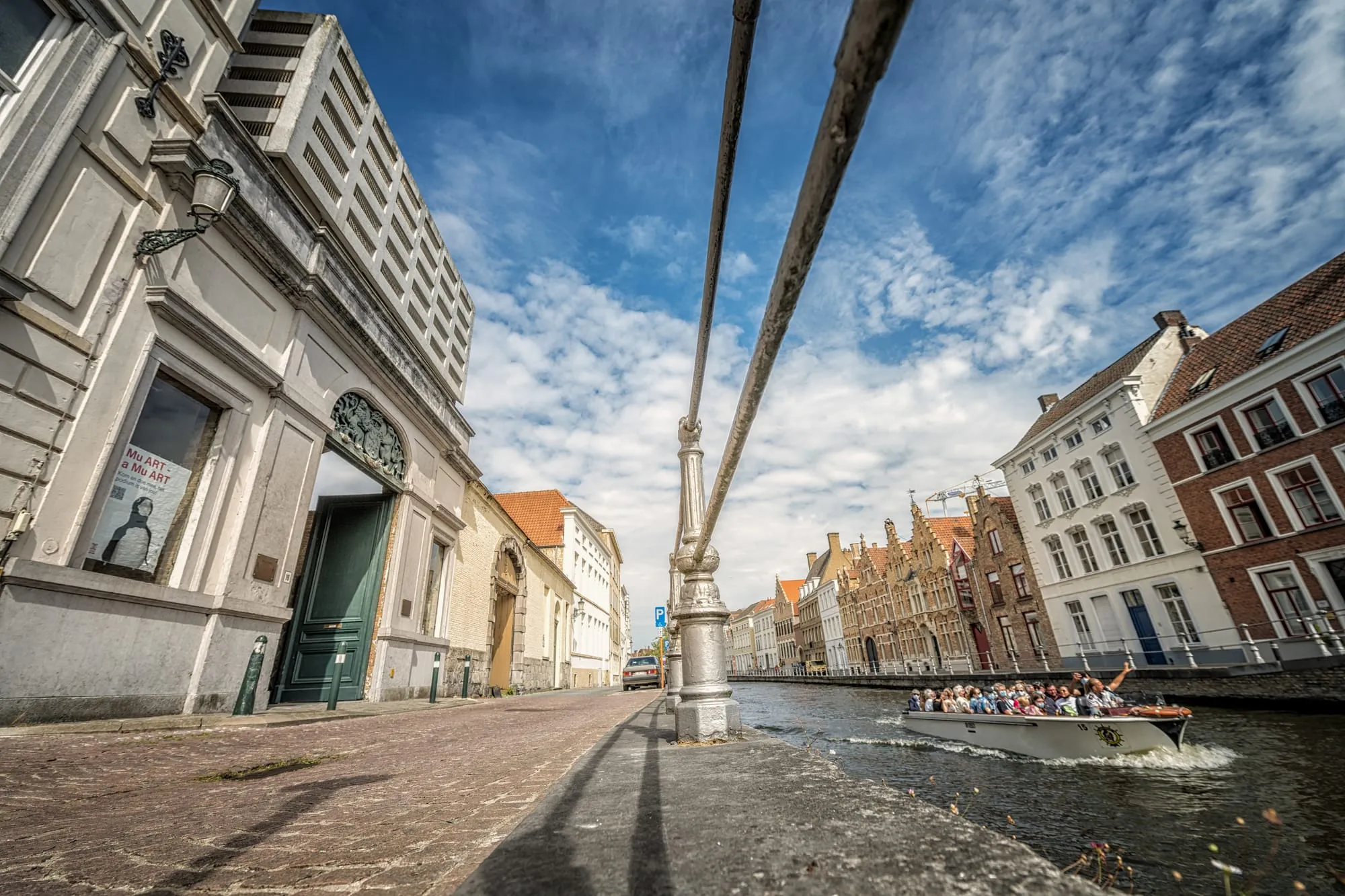 A Bruges canal with a tour boat passing historic guild façades